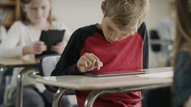 Pan up to boy in classroom reading digital tablet / Provo, Utah, United States