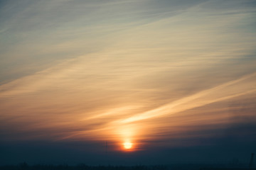 A beautifu multicolored sky at dawn in steam trails from aircraft. The sun is in the center of the horizon.