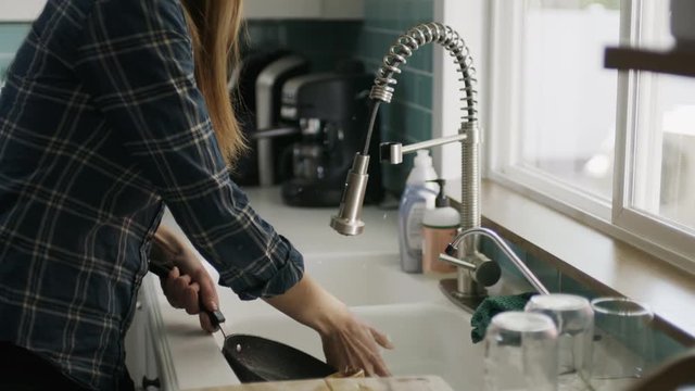 Slow motion of woman washing pan talking on cell phone and dropping it into sink / Alpine, Utah, United States