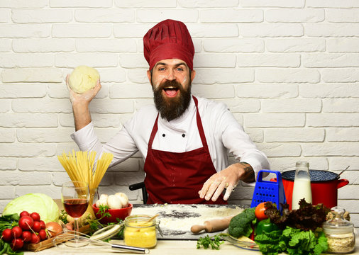 Cook with happy face in burgundy uniform sits by table