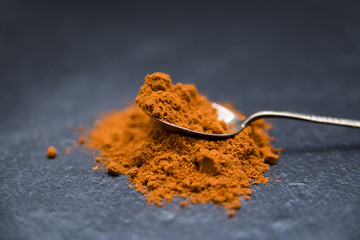 Roter Cayennepfeffer in Pulberform auf einem silbernen Löffelchen auf Schieferpaltte