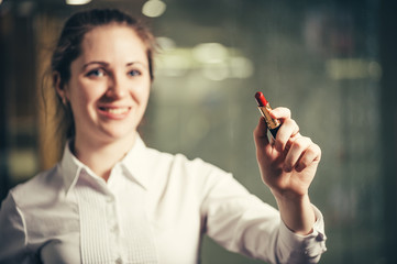 Obraz premium Young girl draws (writes) bright red lipstick on glass. Business woman uses a lipstick instead of a marker.