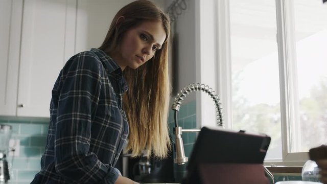 Woman washing dishes while watching streaming video on digital tablet / Alpine, Utah, United States