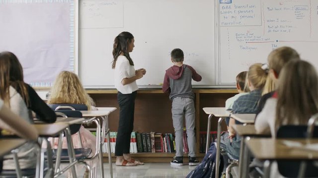 Teacher watching boy solving math equation on classroom whiteboard / Provo, Utah, United States