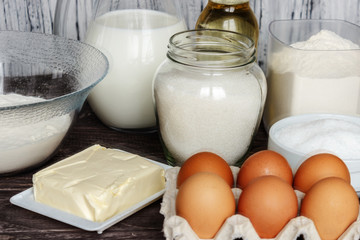 Ingredients for pancakes: milk, eggs, sugar, salt, flour, vegetable oil on a wooden white background.