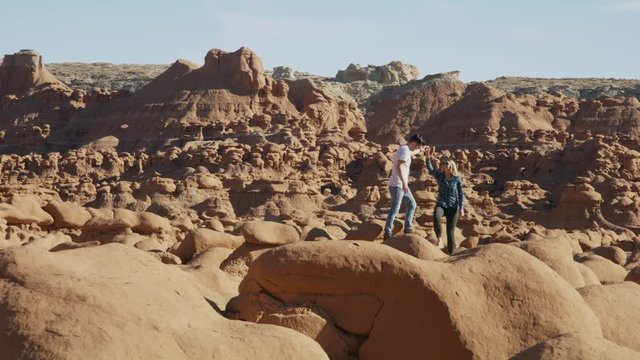 Couple holding hands and walking on rock formations in desert / Goblin Valley, Utah, United States