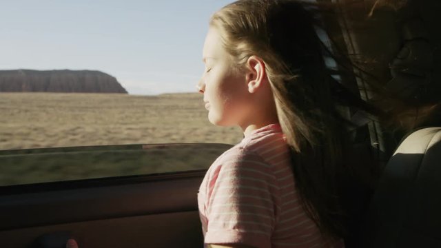 Girl in car leaning out car window enjoying wind blowing hair / Hanksville, Utah, United States