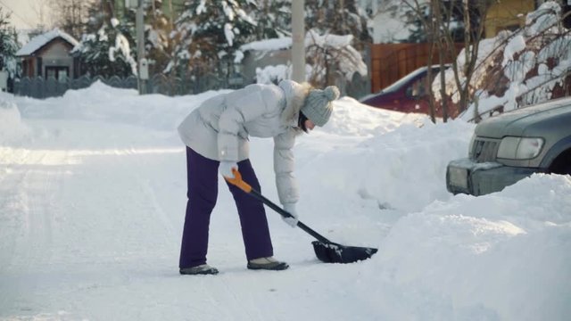 Young woman cleans snow by shovel for car in suburbs in winter.