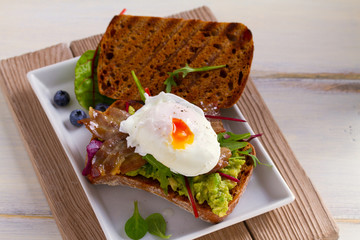 Poached egg, bacon, smashed white bean and avocado on toast. Sandwich. horizontal
