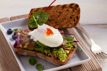 Poached egg, bacon, smashed white bean and avocado on toast. Sandwich. horizontal