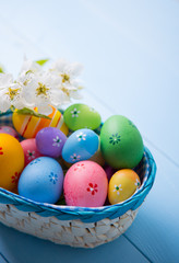 Obraz na płótnie Canvas Variety of decorated colorful Easter eggs in basket with white spring flowers on light blue background