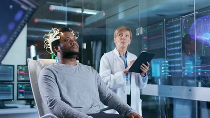In Laboratory Man Wearing Brainwave Scanning Headset Sits in a Chair while Scientist with Tablet Computer Supervises Process. In the Modern Brain Study/ Neurological Research Laboratory. - Powered by Adobe