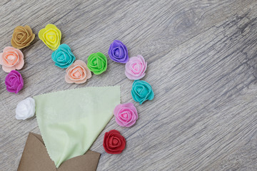 A bright green napkin sticks out of the craft envelope. Decorated in shape of heart with multi-colored roses. Flat lay image.