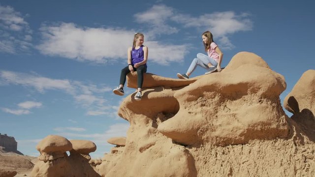 Girl climbing and sitting on the edge of rock formation in desert / Goblin Valley, Utah, United States