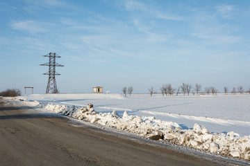 Fototapeta premium Electrical power line pillar on snow in front of blue sky and clouds