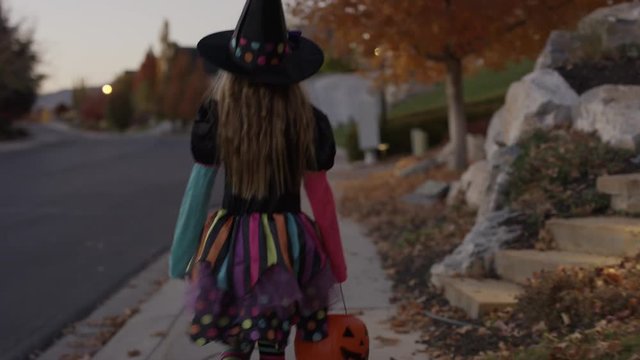 Rear view tracking shot of girl wearing witch costume walking in neighborhood / Cedar Hills, Utah, United States