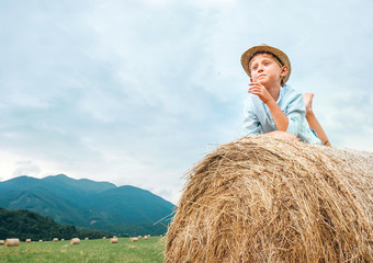 Naklejka na ściany i meble Careless boy lies on hay roll on the mountain field