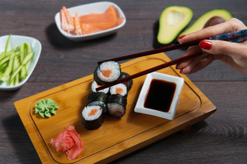 Woman takes the sushi rolls using chopsticks. Black background