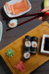 Woman takes the sushi rolls using chopsticks. Black background