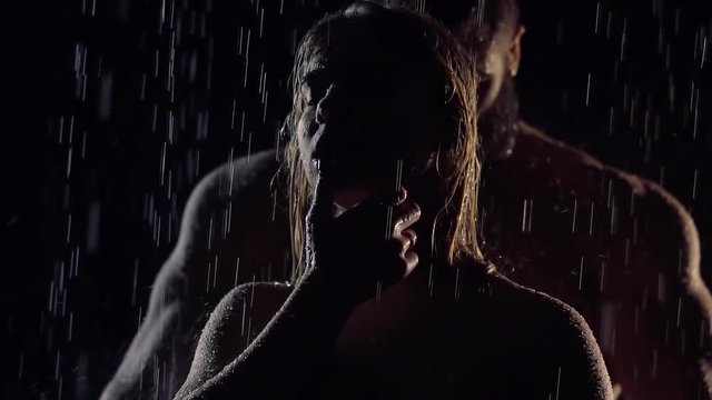 silhouette of frail woman and muscular man behind her back, both standing under rain in night