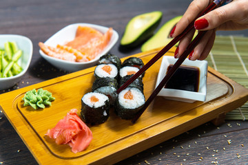 Woman takes the sushi rolls using chopsticks. Black background