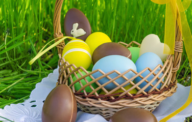 Easter basket with easter chocolate eggs and colored eggs on grass background.