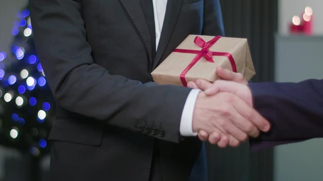Closeup of a man shaking hands and holding a Christmas gift or present. Soft focus