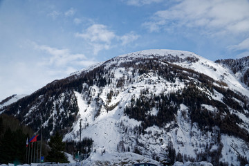 Mountains covered with snow, blue sky with clouds and winter forest near Mont Blanc Alpes, Italy