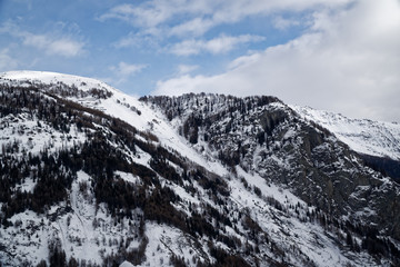 Mountains covered with snow, blue sky with clouds and winter forest near Mont Blanc Alpes, Italy