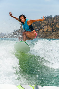 Mixed race fit young woman wakesurfing on a lake in California on a clear summer day