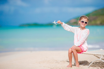 Fototapeta na wymiar Happy little girl with toy airplane in hands on white sandy beach. Kid play with toy on the beach