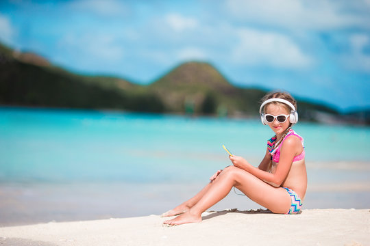 Little adorable girl on the beach listening the music in big headphones