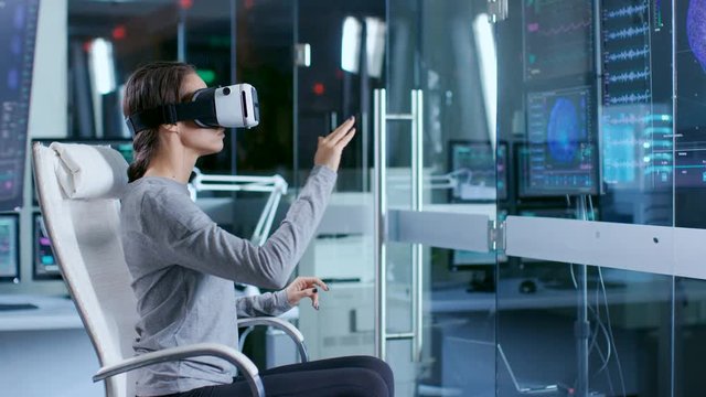 In Laboratory Scientist Wearing Virtual Reality Headset Sitting in a Chair Interacts With Monitors Showing Brain Activity, and Neurological Data. Modern Brain Study/ Neurological Research Center.