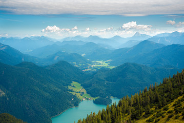 Alpine landscape, wooded slope, lake, distant blue mountain ridge