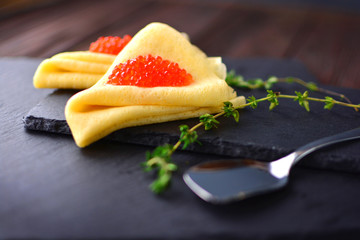 Pancakes with red caviar, decorated with a branch of thyme, on a stone background.