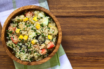 Quinoa salad with sweet corn, olive, tomato, cucumber and chives in wooden bowl, photographed...