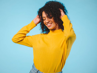 Fototapeta na wymiar Close up portrait of laughing african american woman isolated on blue background. Mix raced girl in yellow wear posing in studio.