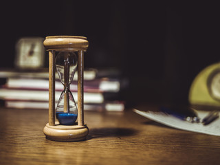 close up of hourglass on the table with clock and books