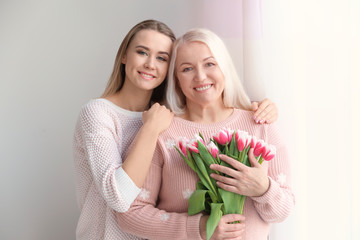 Young daughter and mother with bouquet of flowers at home