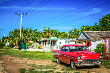 Obraz na płótnie Canvas Roter amerikanischer Oldtimer parkt vor einem Haus im Landesinneren von Santa Clara Kuba - HDR - Serie Cuba Reportage 