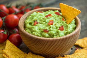 Guacamole in Wooden Bowl with Tortilla Chips and Tomatoes
