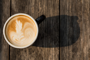 Hot Latte art coffee black cup on Wooden table and wood background texture wallpaper with sun light