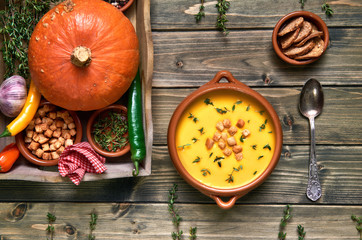 Pumpkin soup in ceramic bowl on rustic wood served with thyme and croutons, with  ingredients around