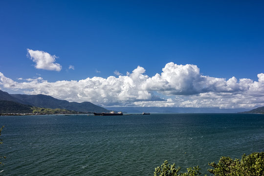 Port of Sao Sebastiao - Sao Paulo, Brazil - seen from Ilhabela with cargo ships docked on sunny day with blue sky with clouds