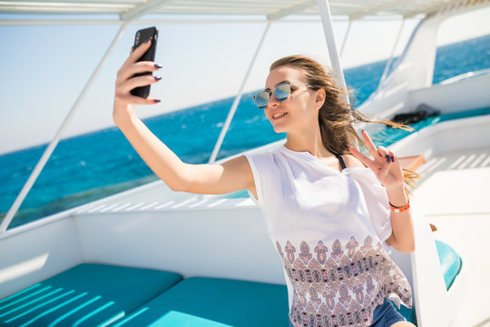 Young beautiful brunette girl making selfie using phone while sitting on the yacht