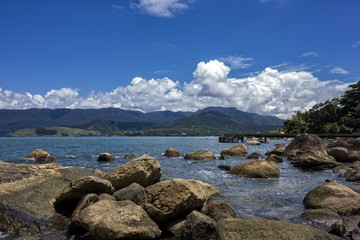 Fototapeta na wymiar View of Juliao beach in Ilhabela - Sao Paulo, Brazil - with rocks in the sea on sunny day with blue sky with clouds