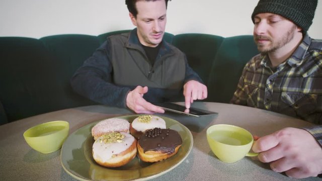Breakfast Meeting Technology Tablet Business Meeting Concept Two 30 Something Men Looking at Screen Paczki Donuts in Foreground