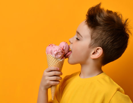 Baby boy kid eating licking strawberry ice cream in waffles cone on yellow 