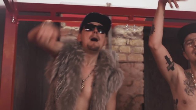Cheeky caucasian hip hop men topless glasses and snapbacks with sexy chiks in underwear standing on bed covered in money rapping