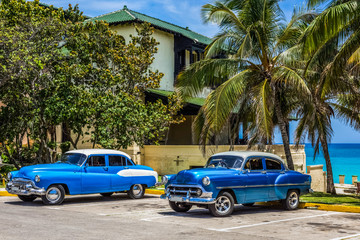 Zwei amerikanischer blau weisse Oldtimer mit weissem Dach parken unter Palmen am Strand von Varadero Kuba - HDR - Serie Cuba Reportage